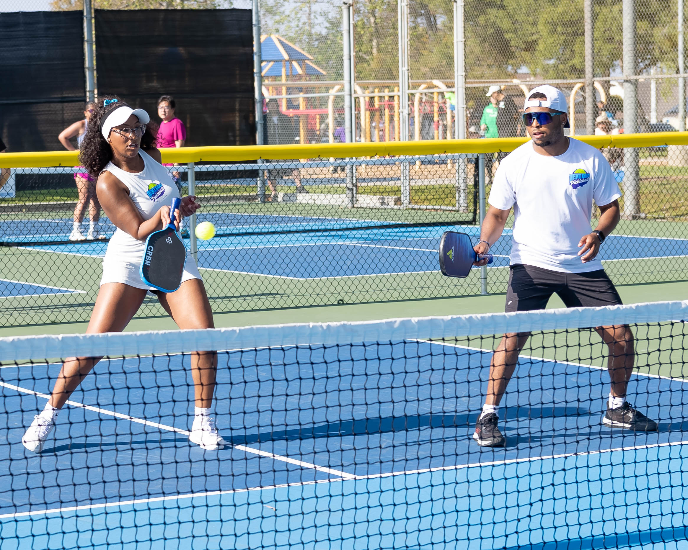 Man and woman playing pickleball on an outdoor court, both holding paddles and focused on the ball.