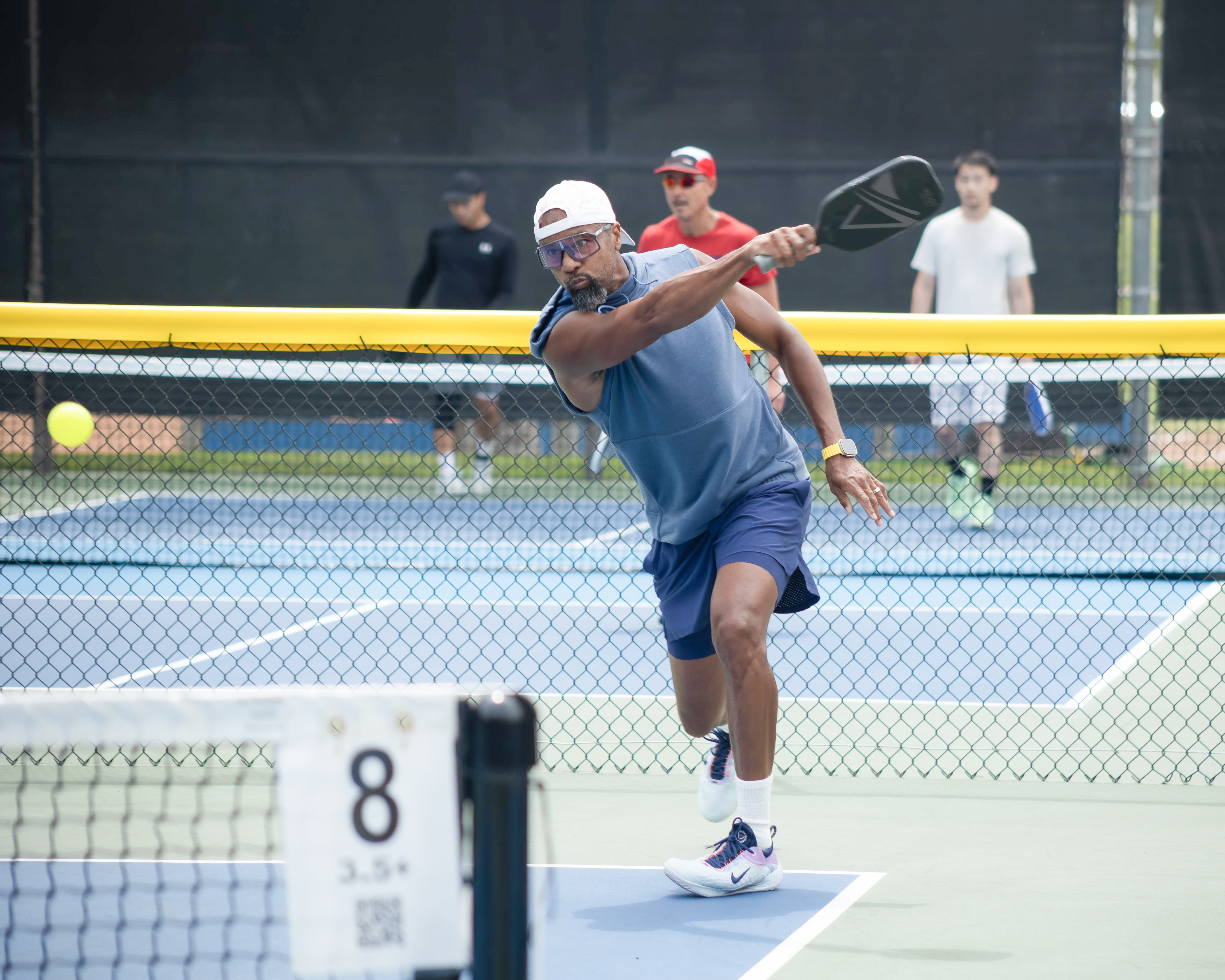 Man in athletic gear hitting a pickleball with a paddle on an outdoor court during a match.