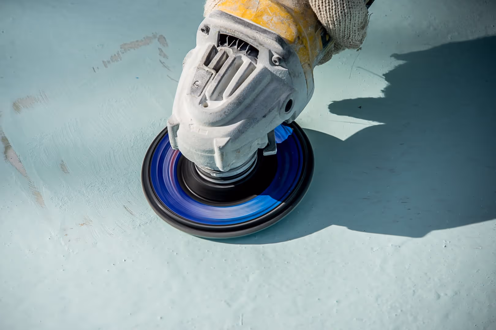 Primer plano de una amoladora angular eléctrica con un disco giratorio azul que pule una superficie azul claro.