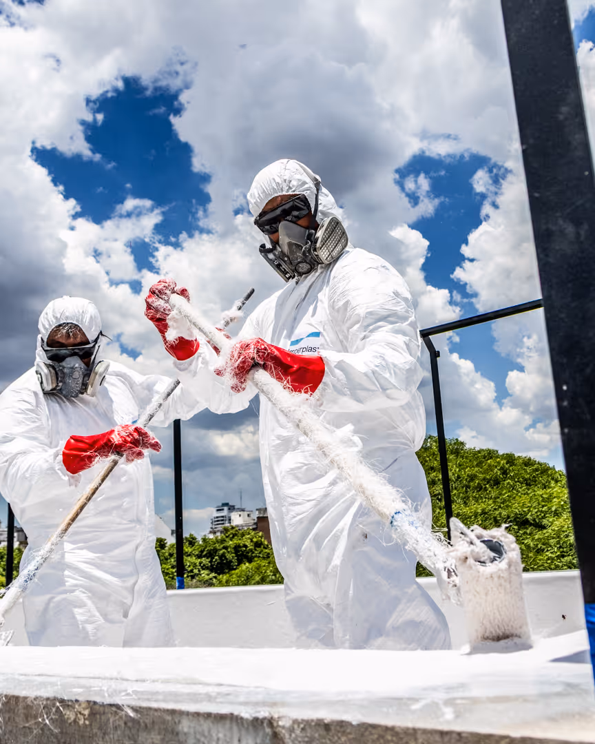 Tres trabajadores con trajes de protección y guantes rojos aplican material de fibra de vidrio dentro de una piscina vacía.