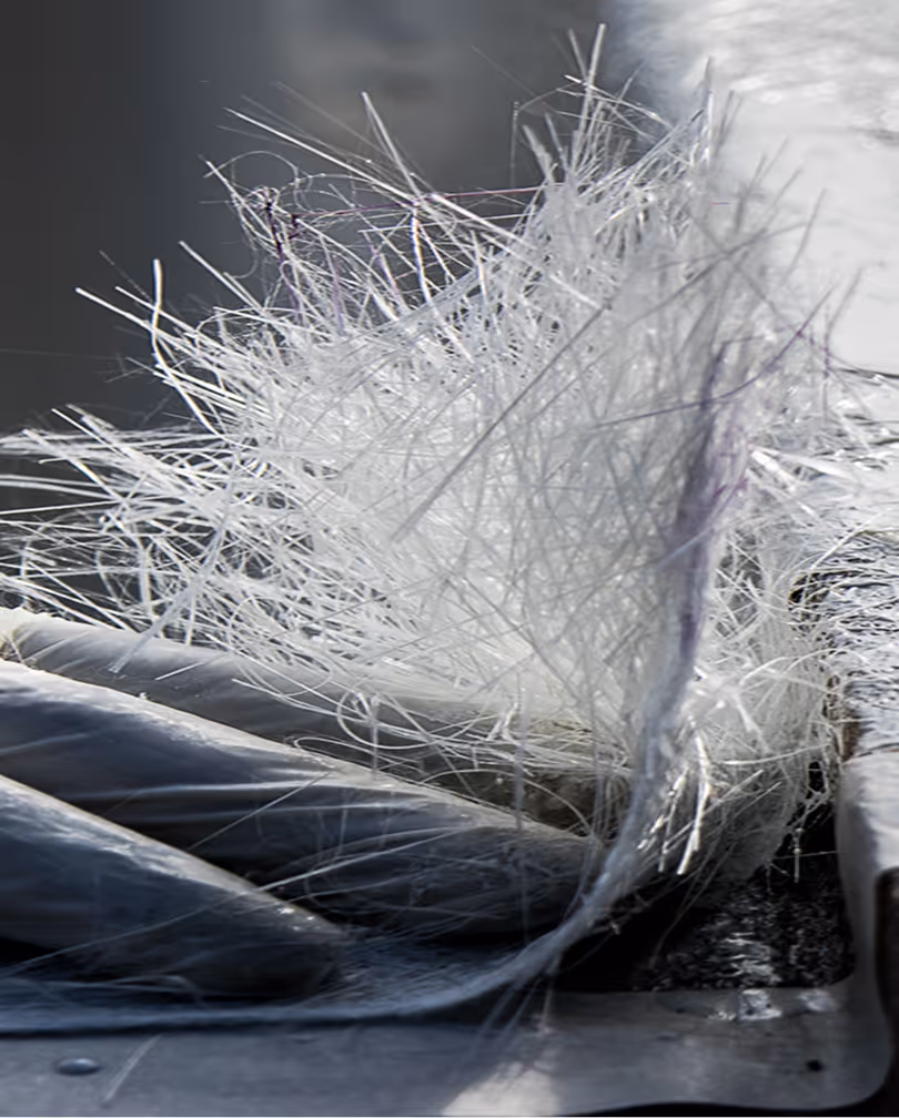 Primer plano de hebras de fibra de vidrio blanca que emergen de una envoltura sobre una superficie metálica.