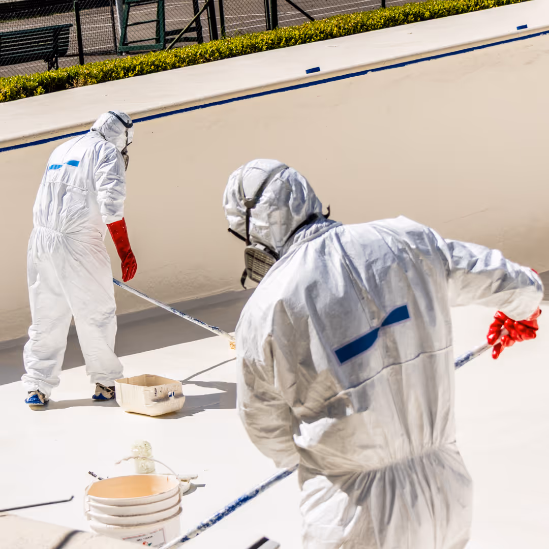 Persona con traje de protección pintando una pared de la azotea con un rodillo.