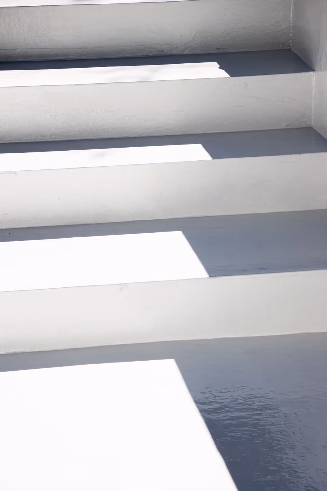 Escaleras pintadas de blanco con sombras rectangulares proyectadas en tres escalones.