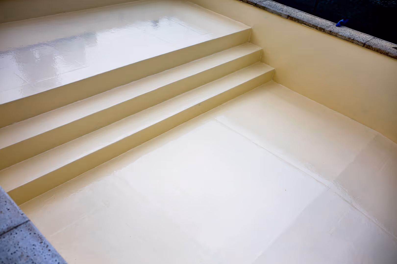 Piscina vacía de color beige con cuatro escalones y superficie lisa y brillante.
