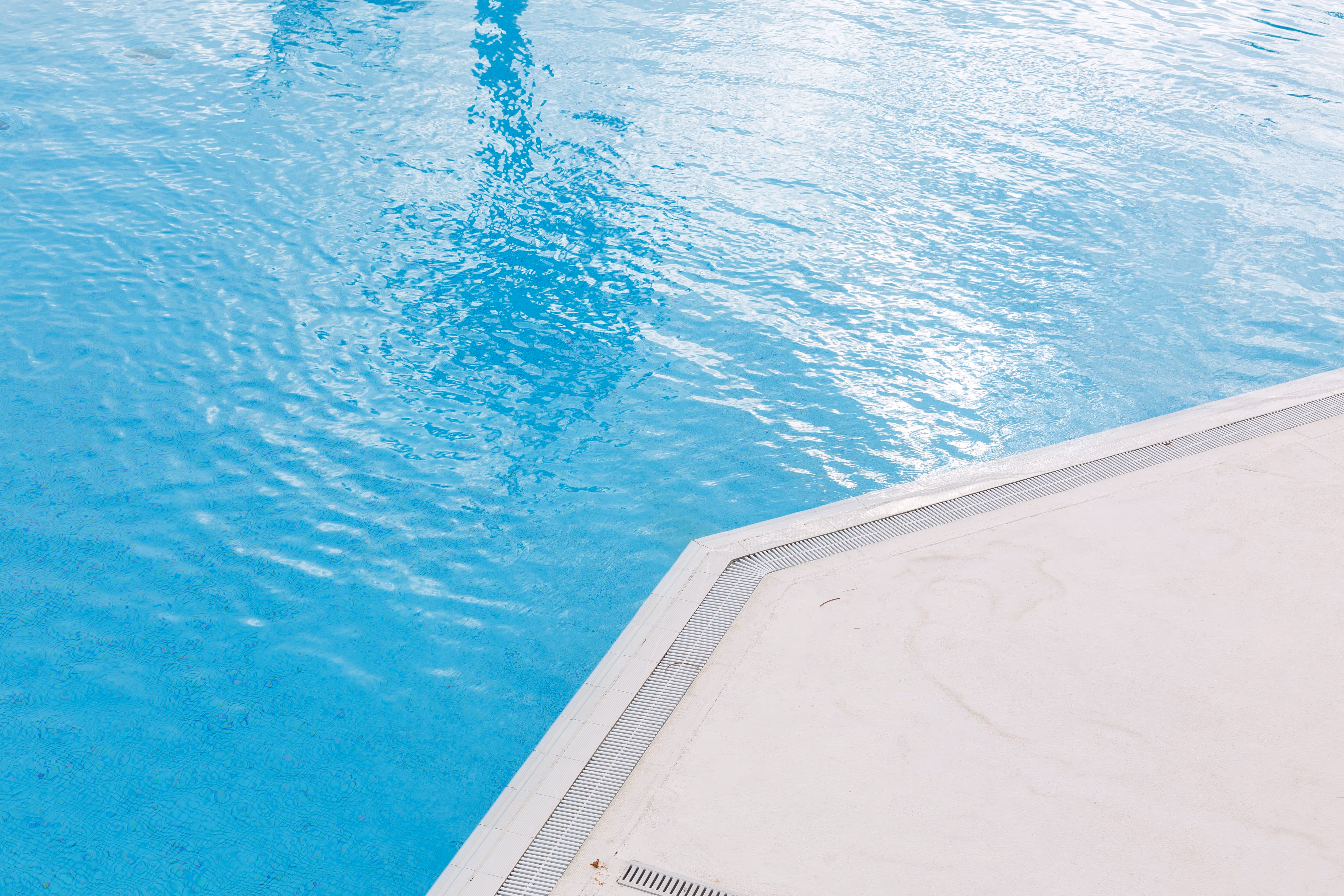 Clear blue swimming pool water with ripples next to a white pool deck.