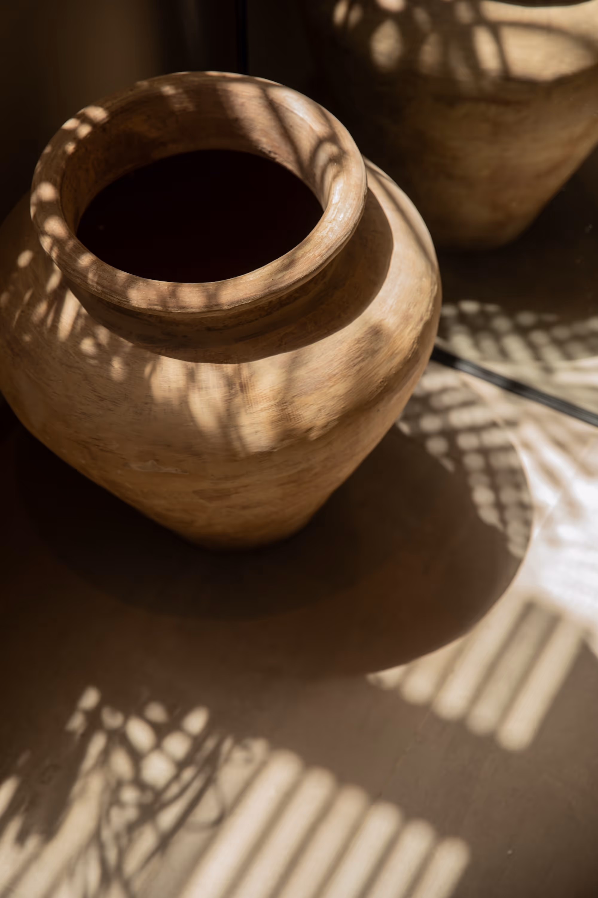 Two rustic clay pots casting patterned shadows on a surface in soft sunlight.