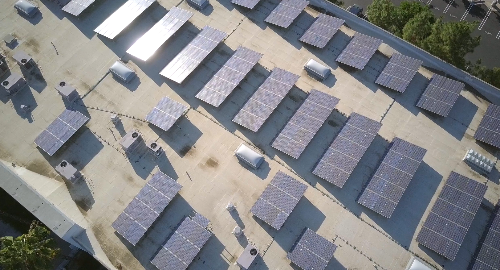 Aerial view of a flat rooftop covered with multiple solar panels and air conditioning units.