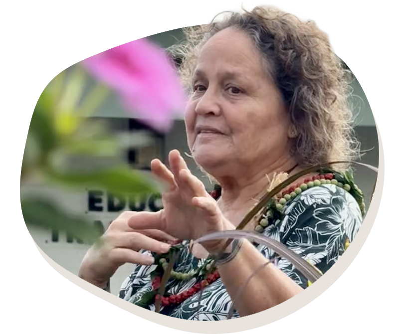 Older woman with curly hair wearing a floral shirt and beaded necklaces gestures with her hands.