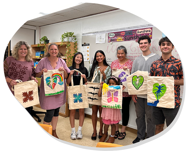Group of eight people holding handmade bags painted with colorful nature-themed designs indoors.