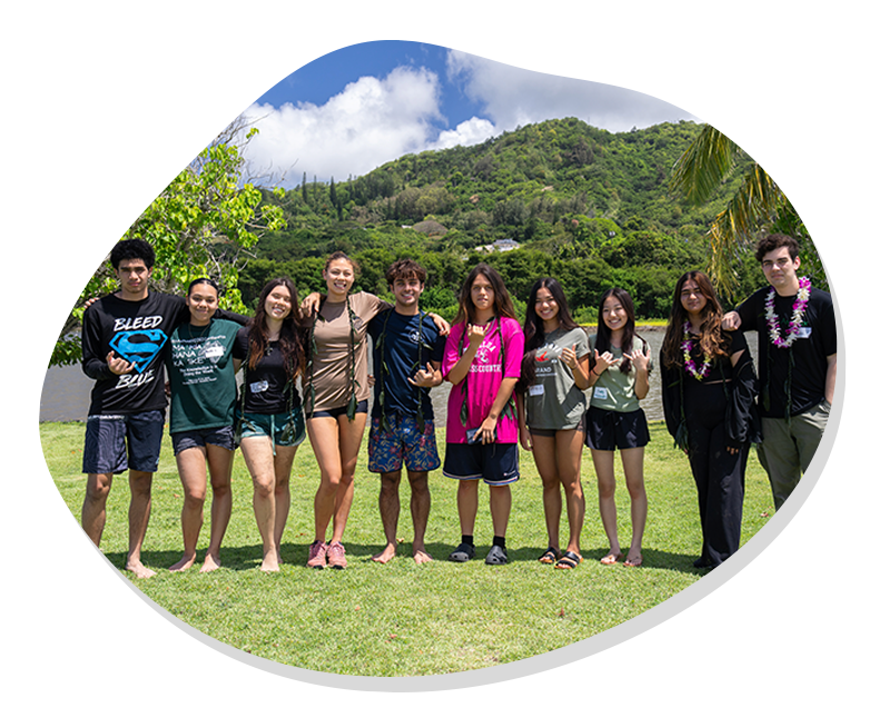 Group of ten diverse young people standing arm in arm on grass with green hills and blue sky behind them.