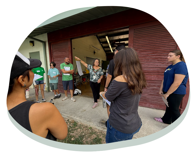 Group of people standing outside a building, listening to a woman holding a large sheet of paper.