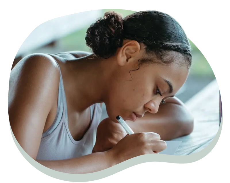 Young woman with braided hair intently writing on paper with a pen at a table.