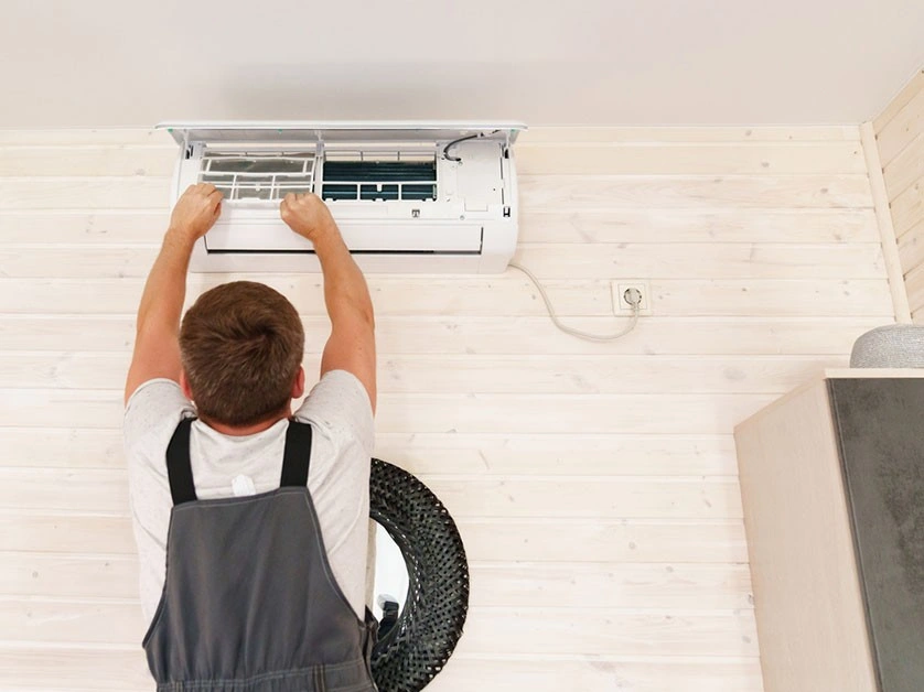 Technician reaching into wall air conditioner.