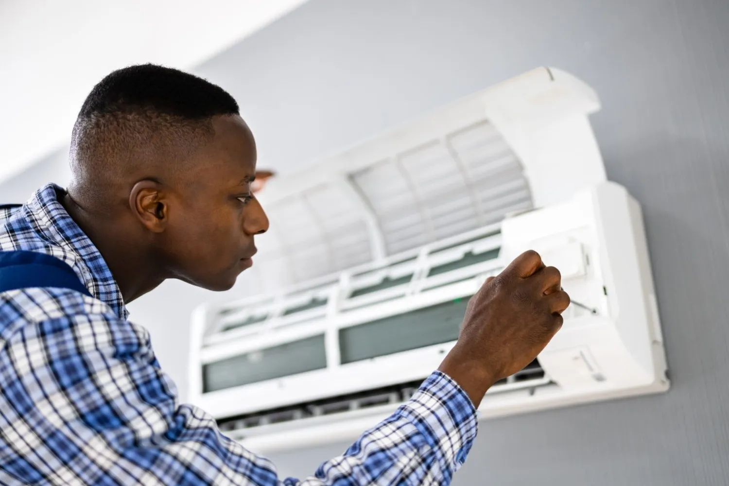 A man inspects and adjusts the settings on a wall-mounted air conditioning unit with its front panel open.