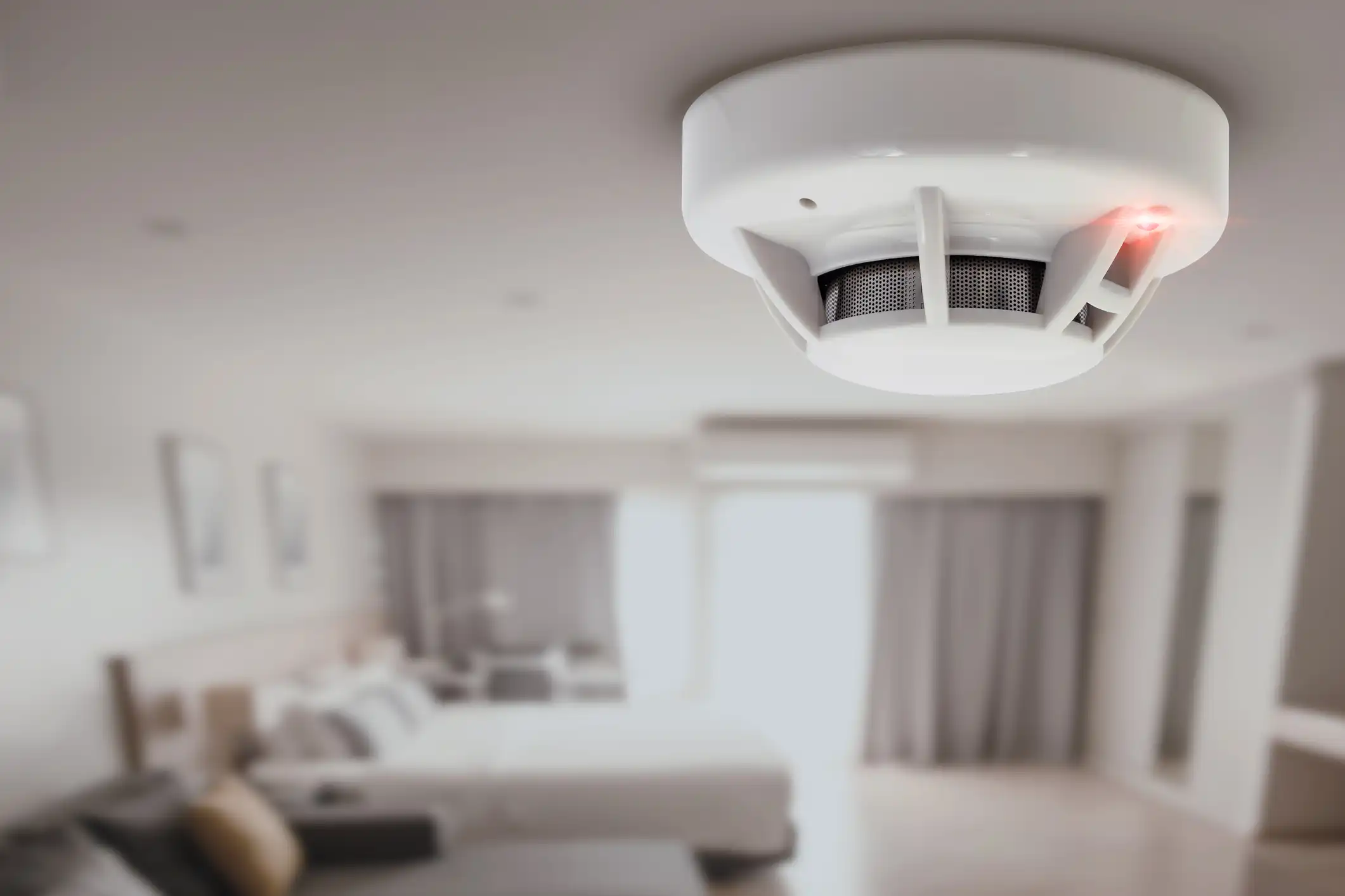 A smoke detector mounted on a ceiling in a modern bedroom.