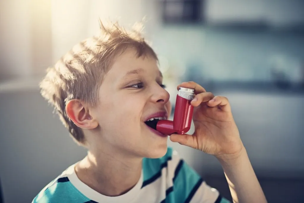 Child using a red inhaler, highlighting asthma management and the importance of indoor air quality for reducing allergy symptoms.