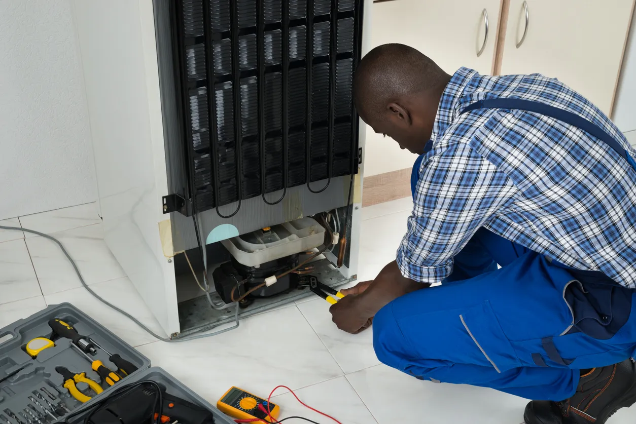 Technician performing refrigerator repair, using tools and multimeter, ensuring quality service for appliance maintenance.