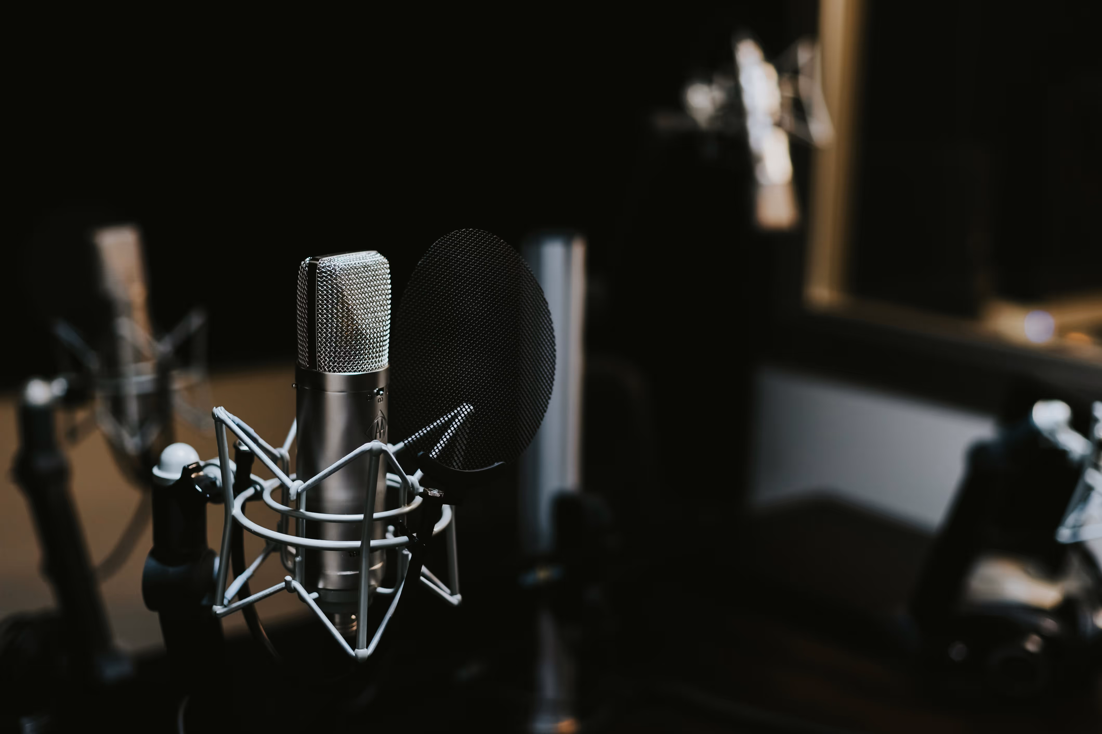 Close-up of a professional silver studio microphone with pop filter in a dark recording studio.