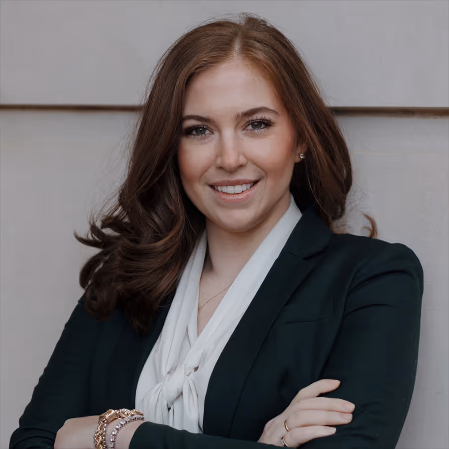 Smiling woman with brown hair wearing a dark blazer and white blouse, arms crossed.