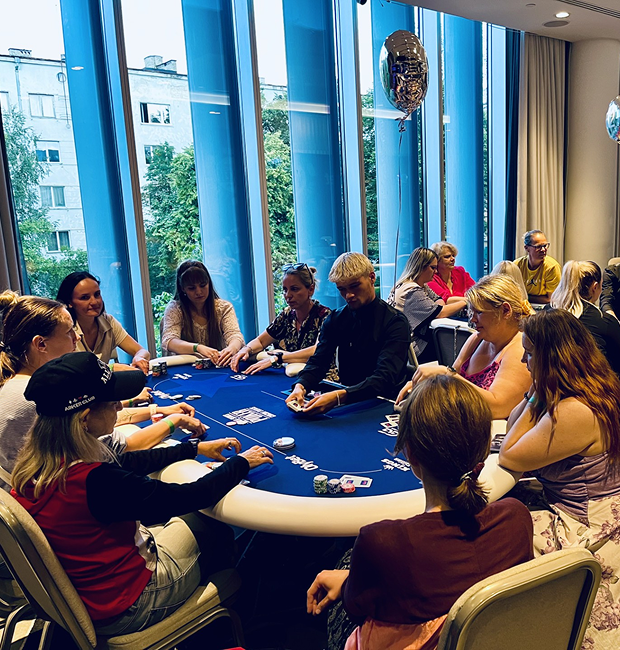 Attendees participating in a live poker workshop event, seated around a blue poker table in a modern conference space.