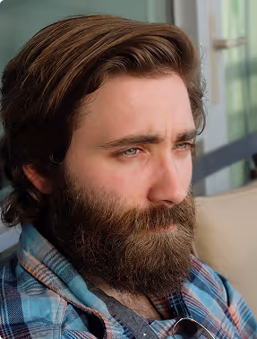 Close-up of a bearded man with brown hair wearing a plaid shirt, looking thoughtfully to the side.