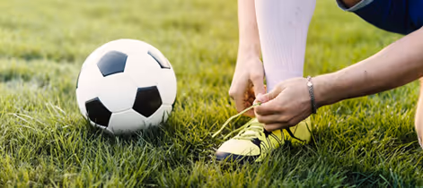 Person tying shoelaces of neon green soccer cleats with a black and white soccer ball on grass.