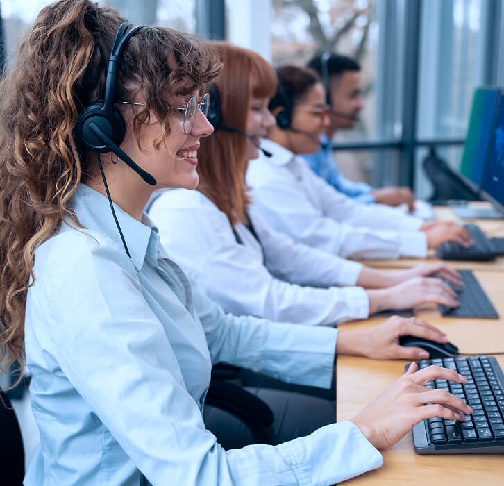 Four customer service representatives wearing headsets and working on computers in an office.