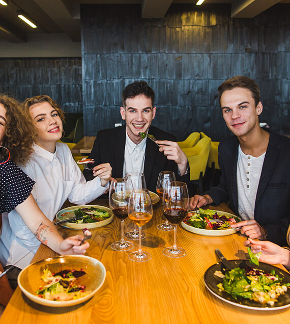 Group of young adults enjoying a meal together at a wooden table with salad plates and wine glasses.