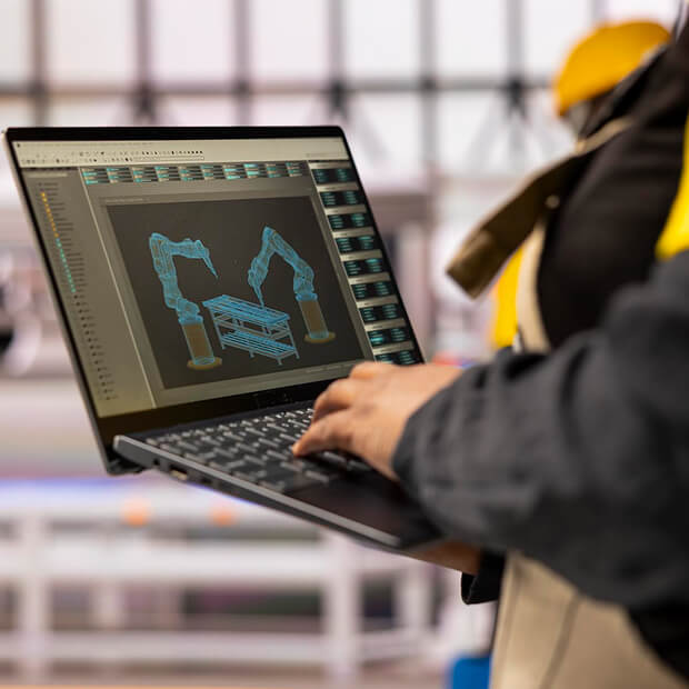 Person using a laptop displaying a 3D CAD design of robotic arms assembling a structure.