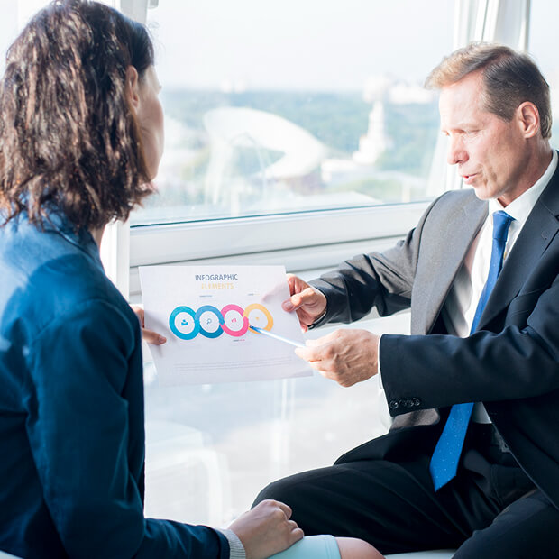 Businessman in suit explaining infographic chart to colleague in office by window.