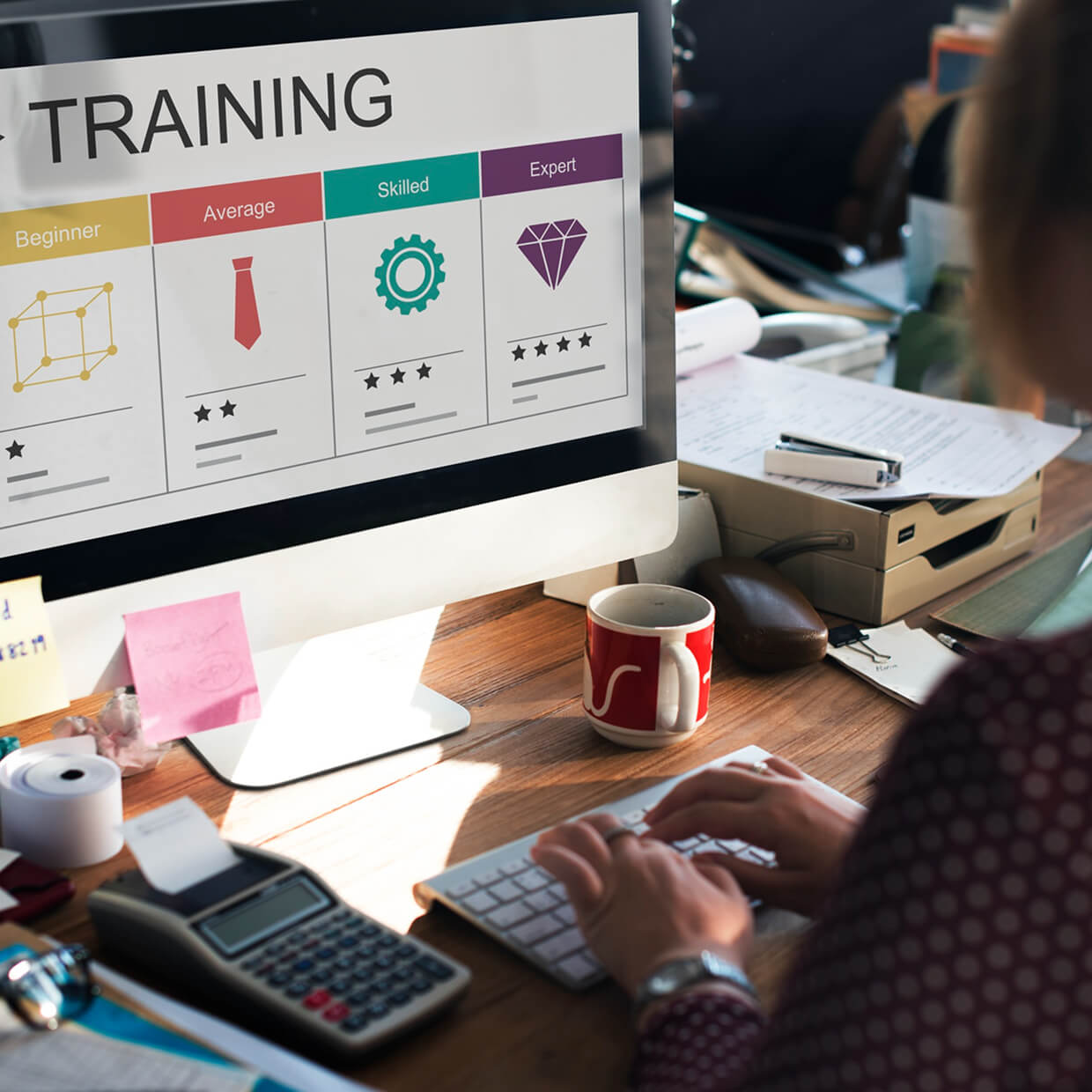 Person typing on a keyboard at a desk with a computer screen showing a training skill level chart from Beginner to Expert.