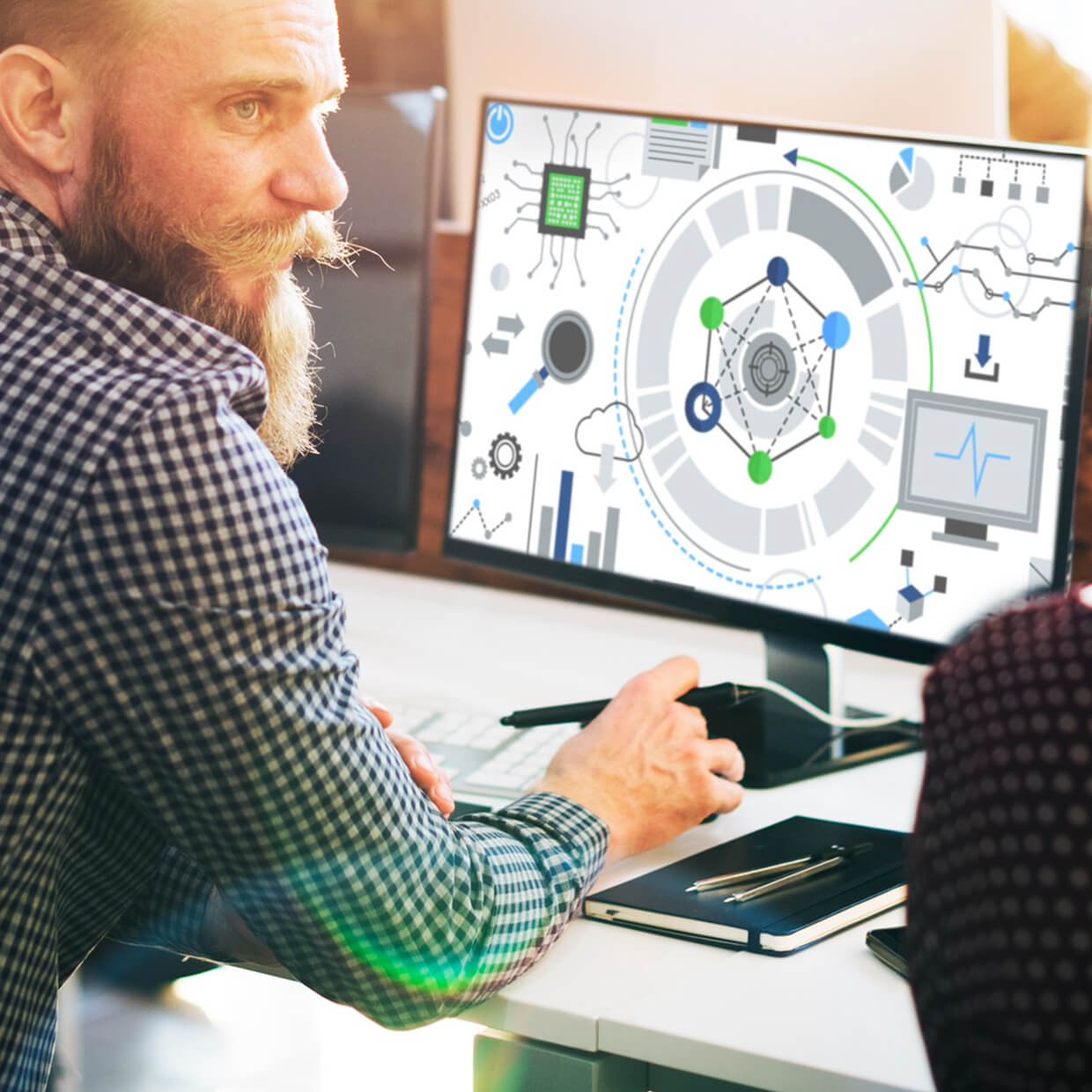 Bearded man in a checkered shirt working on a computer displaying digital technology and data analysis graphics.