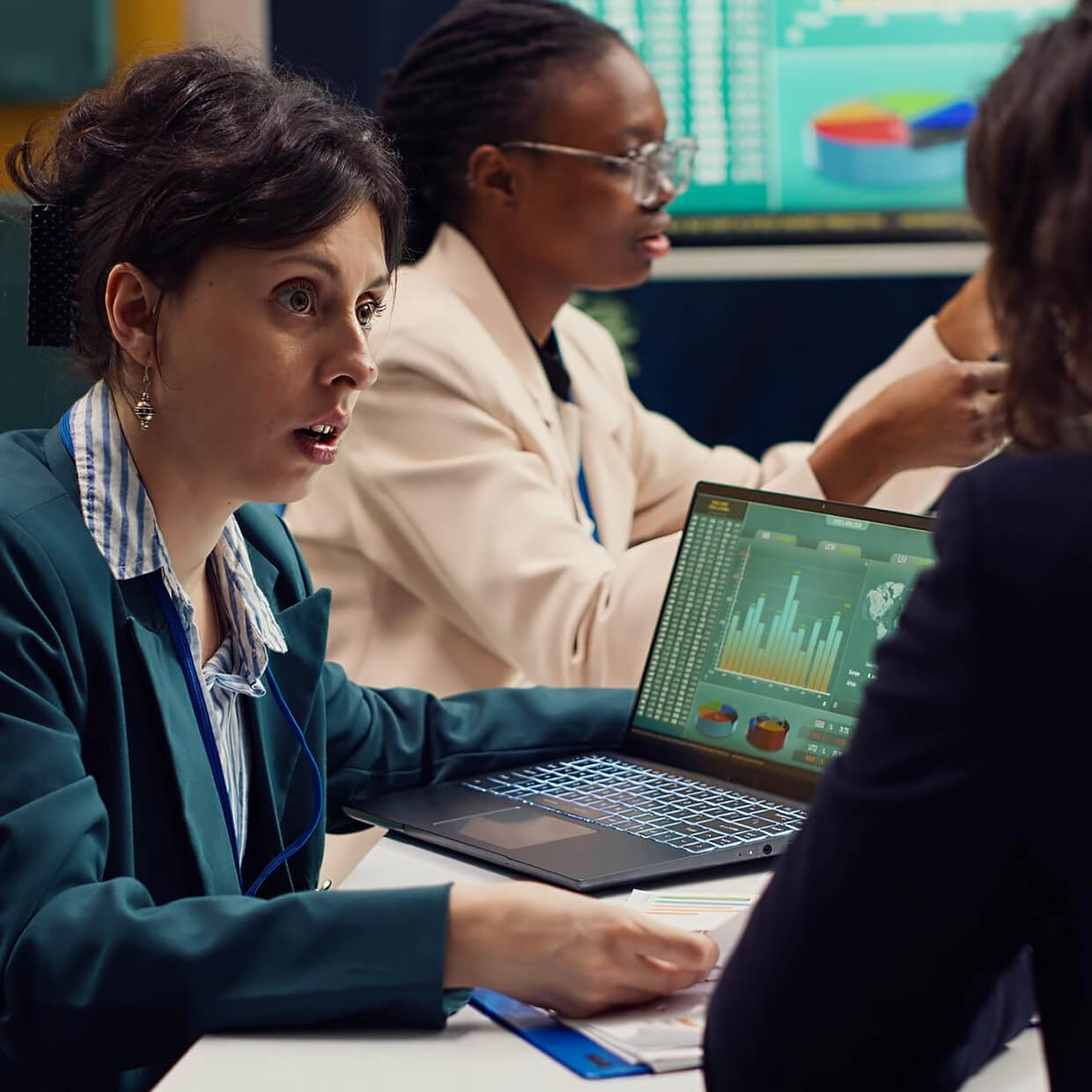 Three professionals engaged in a business discussion with a laptop displaying data charts and graphs on the table.