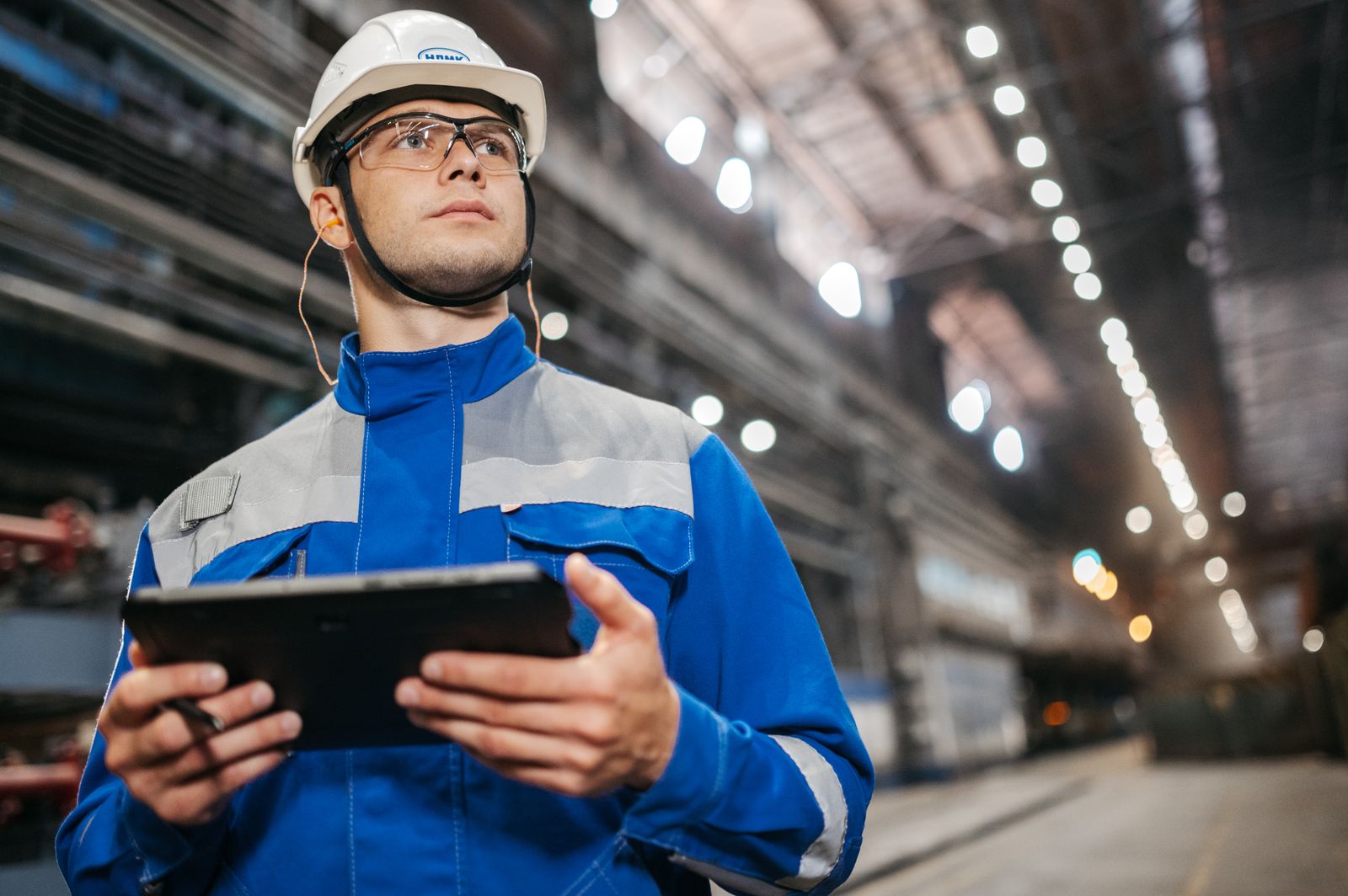 Manufacturing technician in PPE reviewing work on a tablet inside a modern industrial facility