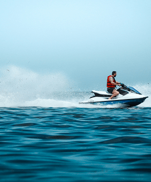 Man wearing a red life jacket riding a jet ski on the ocean with splashing water.