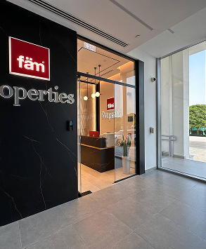 Entrance of a modern office with glass door, black reception desk, and a red illuminated sign reading 'fam' Properties.