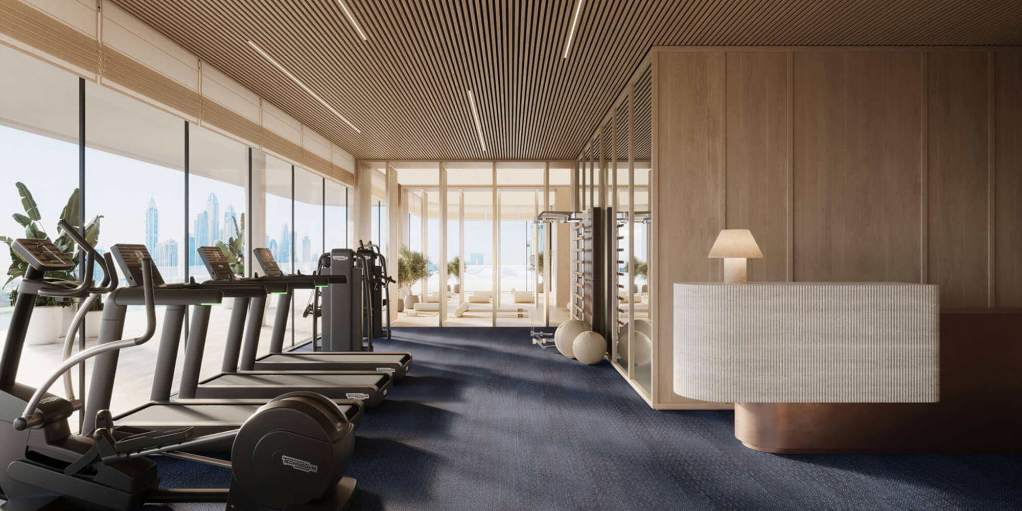 Modern gym interior with treadmills, exercise machines, large windows showing city skyline, and a reception desk with a lamp.