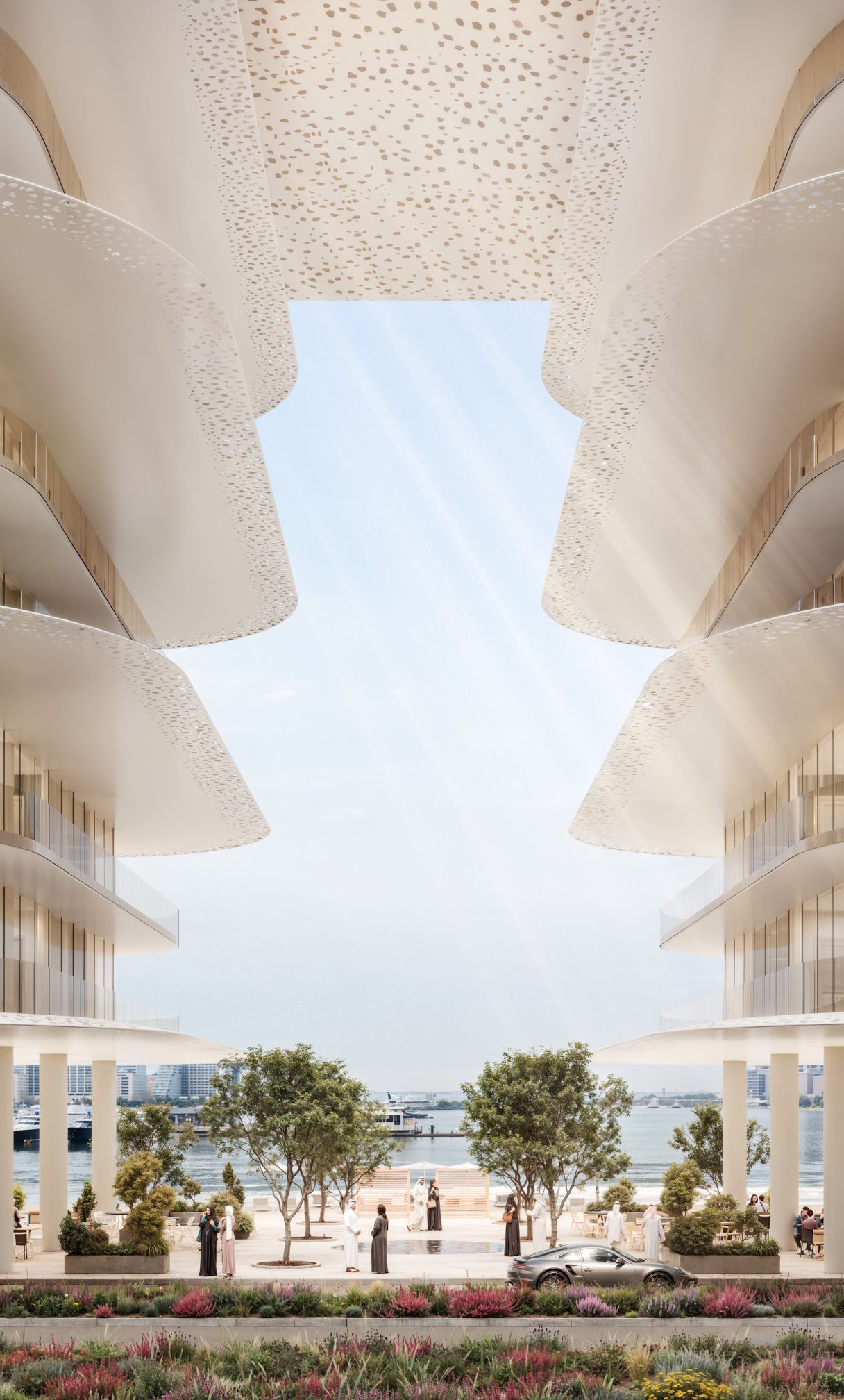 Modern waterfront promenade with stylish curved buildings, landscaped greenery, people walking, and a parked sports car.