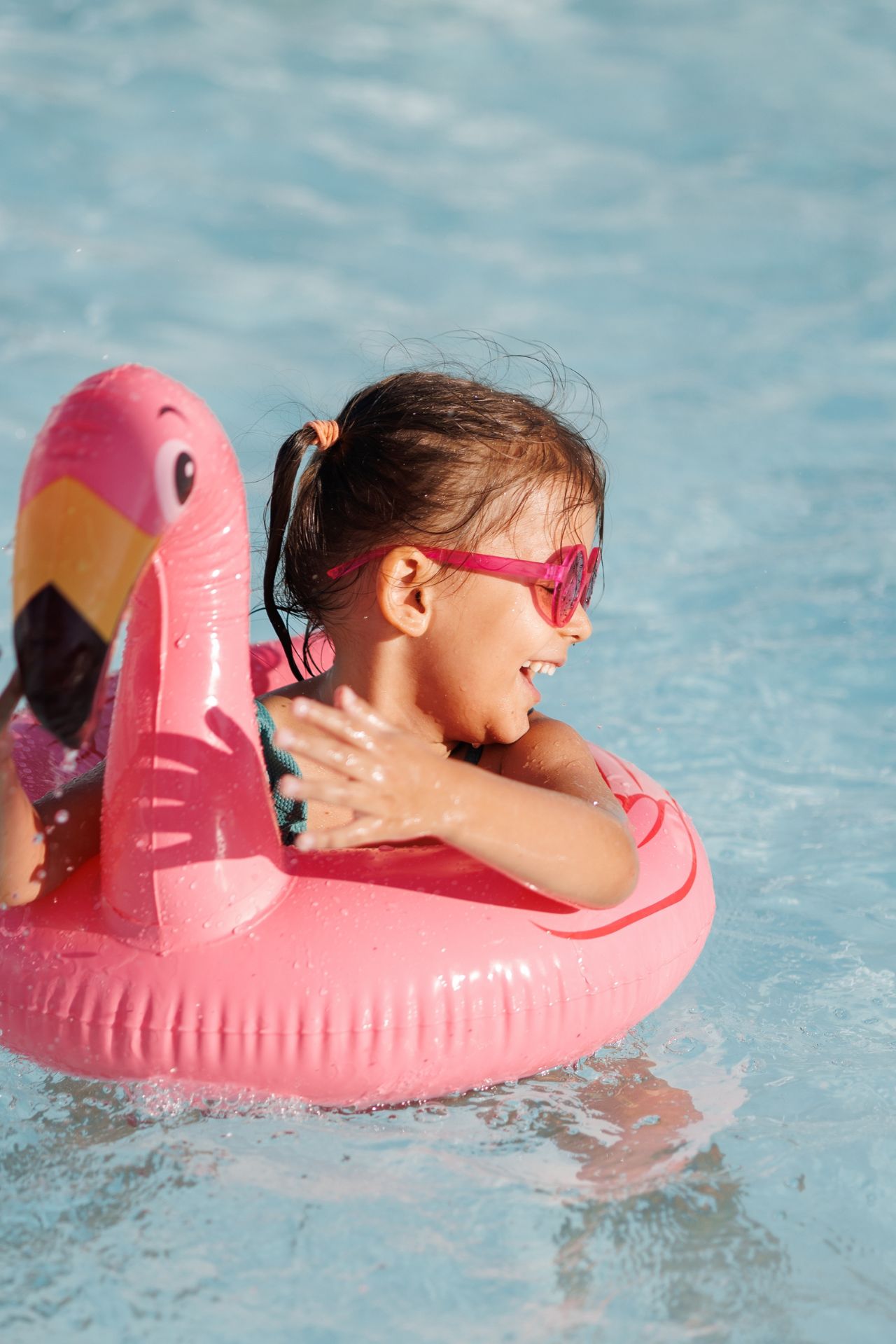 Child wearing pink sunglasses playing in a pool with a pink flamingo float.