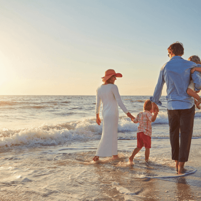 Family of four walking barefoot on the beach near the ocean at sunset.