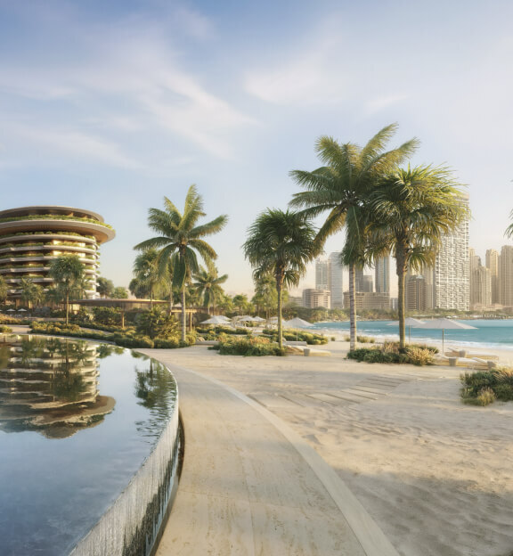 Beachside walkway bordered by palm trees and a curved reflecting pool, with a modern round building and city skyline in the background under a partly cloudy sky.