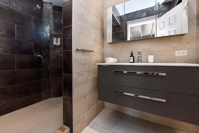 Modern bathroom with dark tile walk-in shower, floating vanity with dark wood drawers, white countertop, and a large mirror.