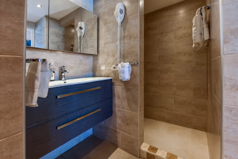 Modern bathroom with beige tiled walls, a dark wood vanity with silver handles, a wall-mounted hairdryer, and a walk-in shower area.