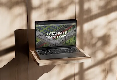 MacBook Pro displaying the 'Sustainable Transport' homepage design, featuring a detailed isometric illustration of electric trains and solar farms.