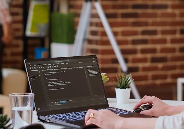 Developer coding custom website backend on a laptop in a modern office, highlighting web development services.