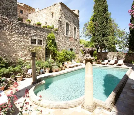 Stone courtyard with a rectangular swimming pool surrounded by lounge chairs and greenery beside an old stone building.