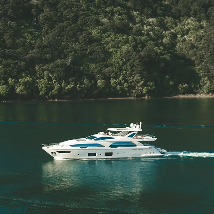 White luxury yacht cruising on calm water with forested shoreline in the background.