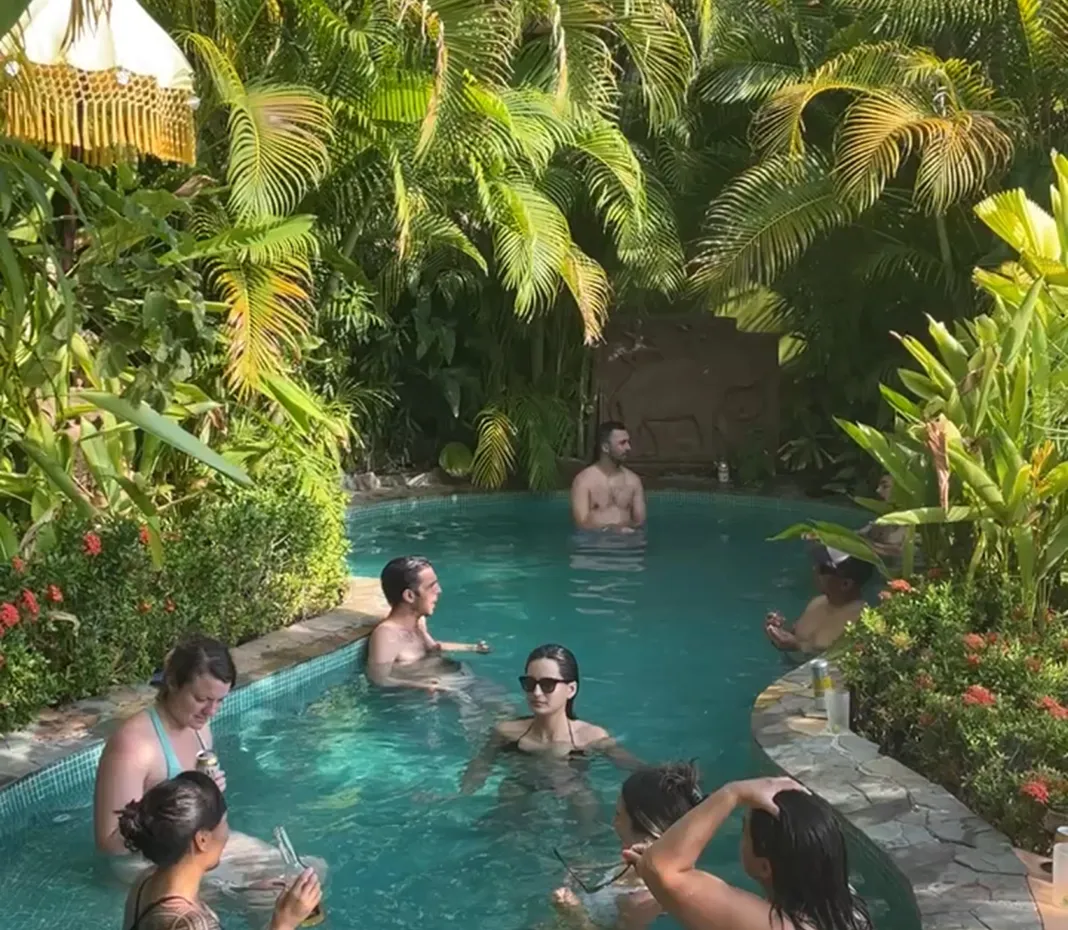 People relaxing and socializing in a small outdoor pool surrounded by lush tropical plants.