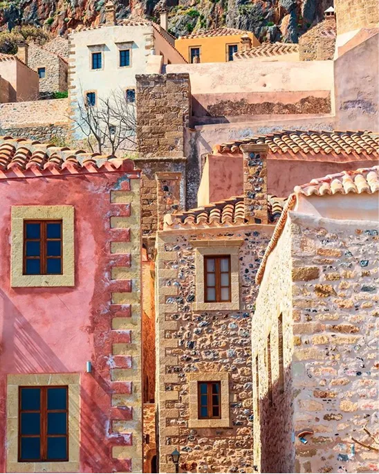 Close-up view of colorful Mediterranean stone buildings with tiled roofs and wooden windows under a rocky hillside.