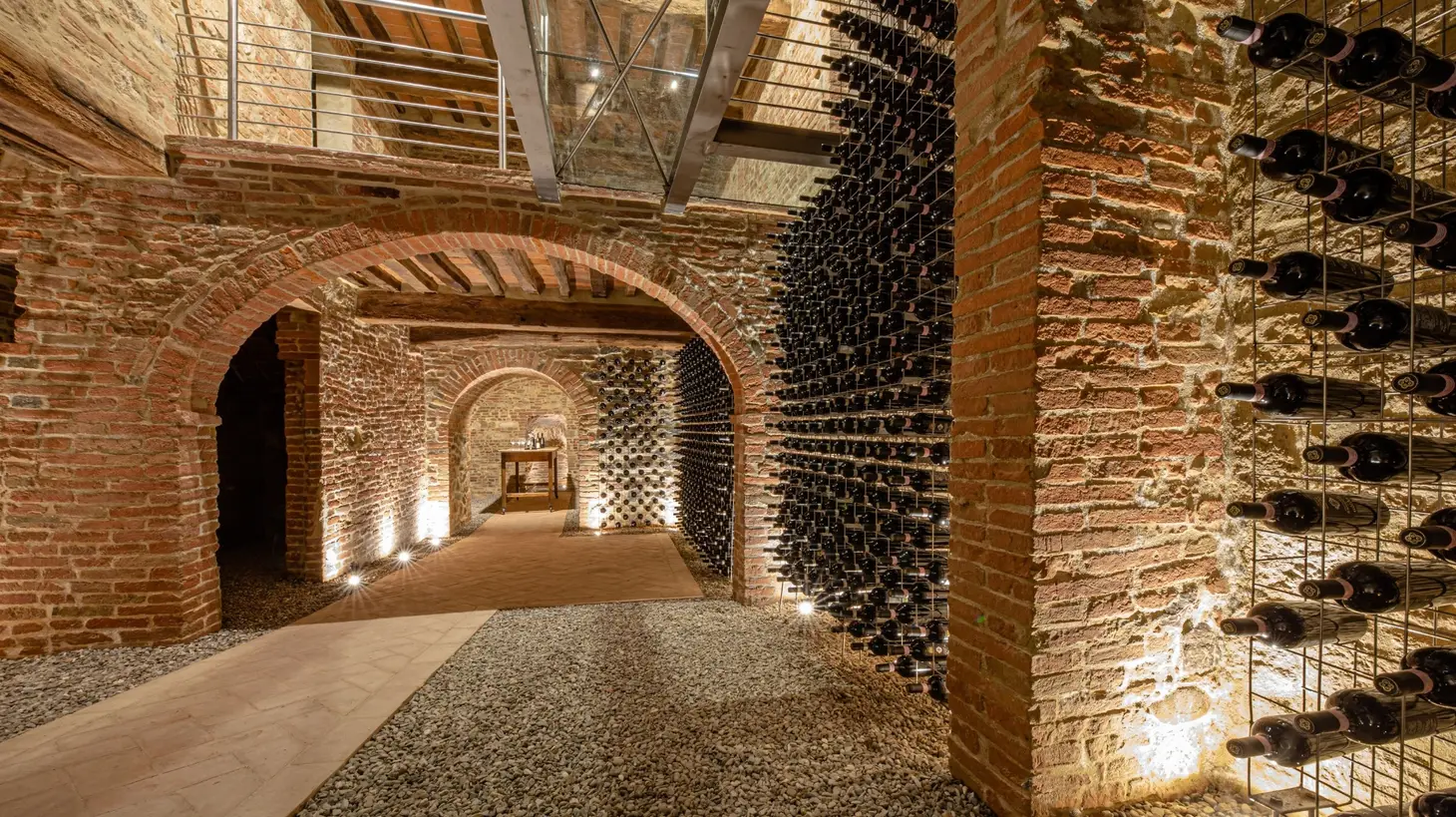 Brick wine cellar with arched doorways and walls lined with racks holding numerous wine bottles.
